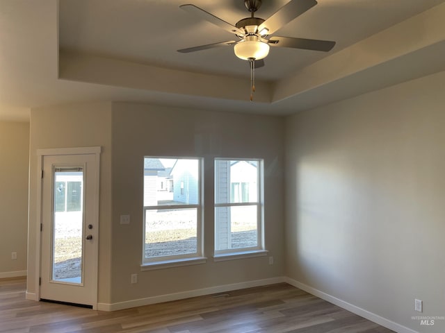 interior space with a wealth of natural light, a tray ceiling, baseboards, and wood finished floors