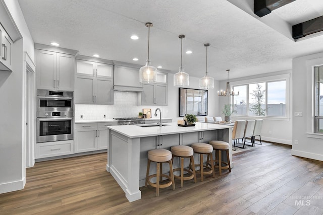 kitchen with pendant lighting, premium range hood, dark wood-type flooring, double oven, and a chandelier