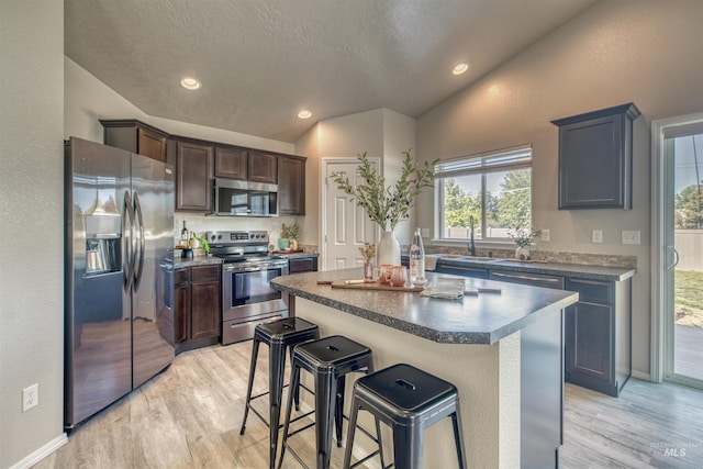 kitchen featuring lofted ceiling, a kitchen breakfast bar, light wood-type flooring, a sink, and stainless steel appliances