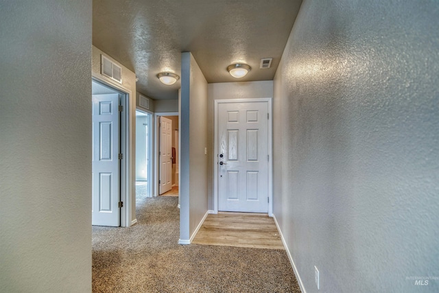 hall with baseboards, a textured wall, carpet flooring, and visible vents