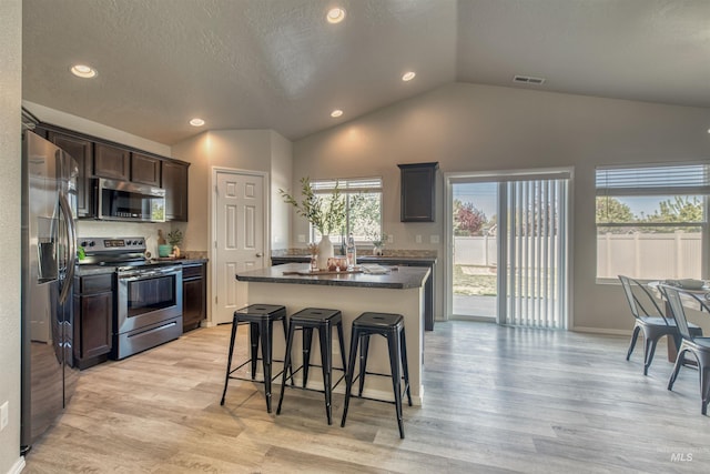 kitchen featuring dark brown cabinetry, visible vents, appliances with stainless steel finishes, a center island, and vaulted ceiling