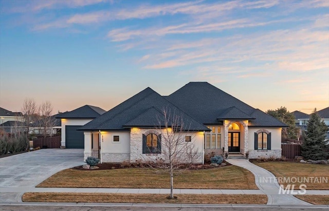 french country style house with driveway, stone siding, fence, and a yard