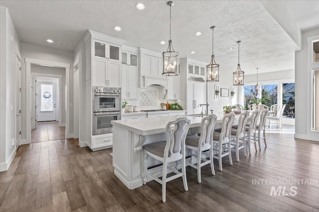 kitchen with tasteful backsplash, a large island, light countertops, stainless steel double oven, and gas stovetop