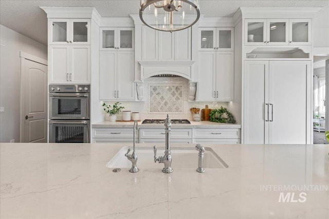 kitchen featuring white cabinets, appliances with stainless steel finishes, light stone countertops, tasteful backsplash, and glass insert cabinets