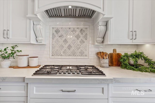 kitchen with wall chimney exhaust hood, tasteful backsplash, white cabinets, and stainless steel gas stovetop