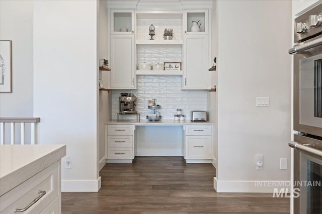 kitchen featuring white cabinets, light countertops, dark wood-style floors, tasteful backsplash, and glass insert cabinets