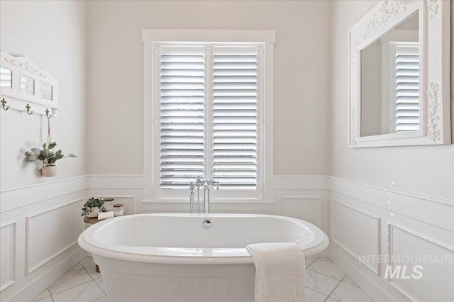 bathroom featuring a soaking tub, wainscoting, a decorative wall, and marble finish floor