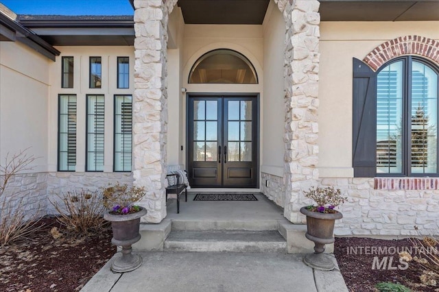 doorway to property with stone siding, stucco siding, and french doors