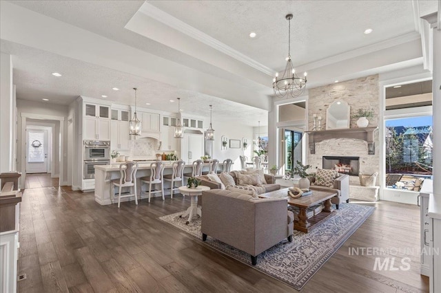 living area featuring an inviting chandelier, a fireplace, a tray ceiling, and dark wood finished floors