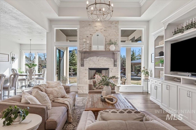 living room featuring crown molding, a fireplace, wood finished floors, and a notable chandelier