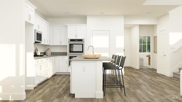 kitchen with stainless steel appliances, light hardwood / wood-style floors, a breakfast bar, white cabinets, and a center island with sink