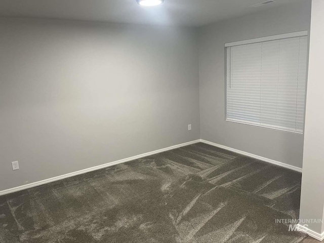 spare room with baseboards and dark colored carpet