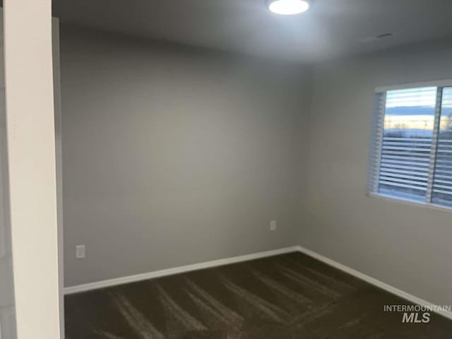 spare room featuring baseboards and dark colored carpet