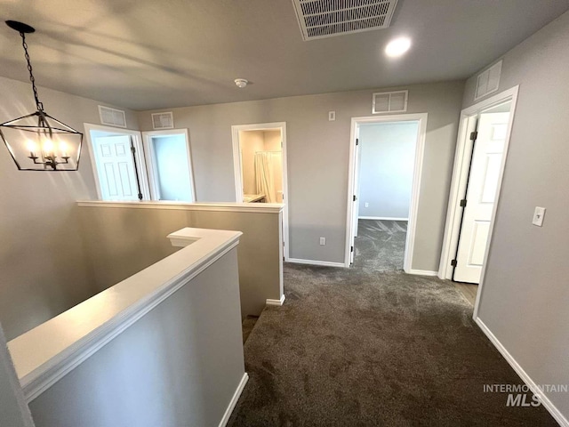 hall with dark colored carpet, visible vents, baseboards, and an inviting chandelier