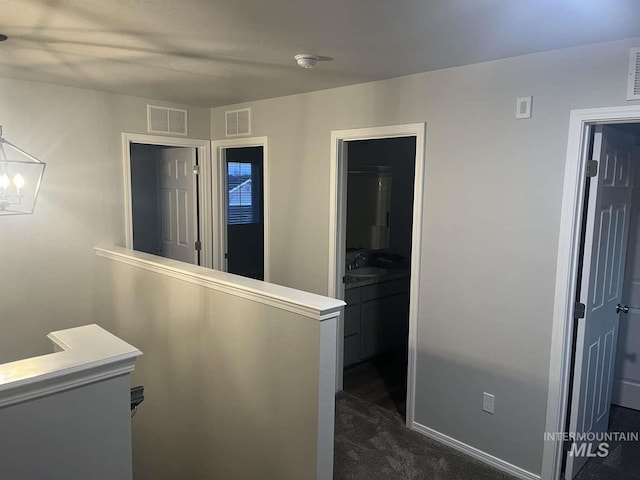 hall with visible vents, dark colored carpet, and a sink