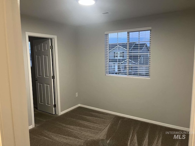 unfurnished room with baseboards and dark carpet