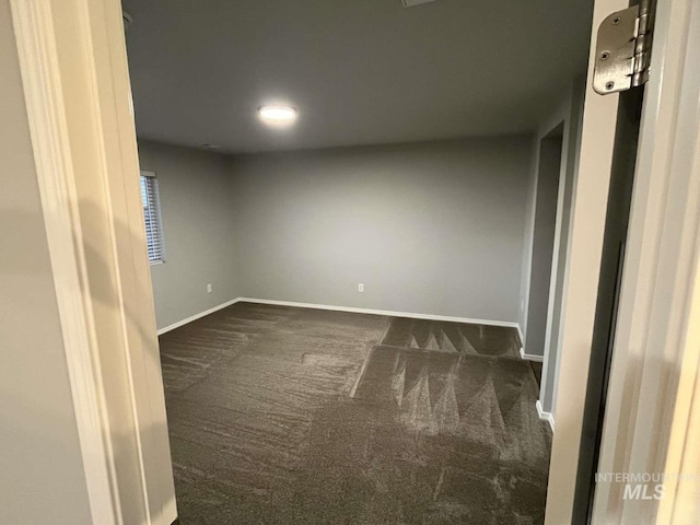 unfurnished room with baseboards and dark colored carpet