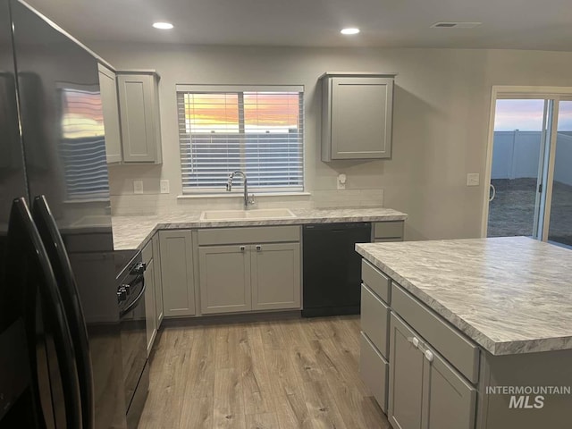 kitchen featuring light wood-type flooring, black appliances, a sink, and gray cabinetry