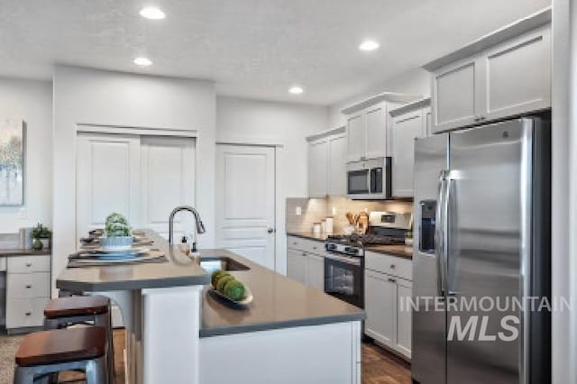 kitchen with a kitchen bar, stainless steel appliances, sink, and a center island with sink