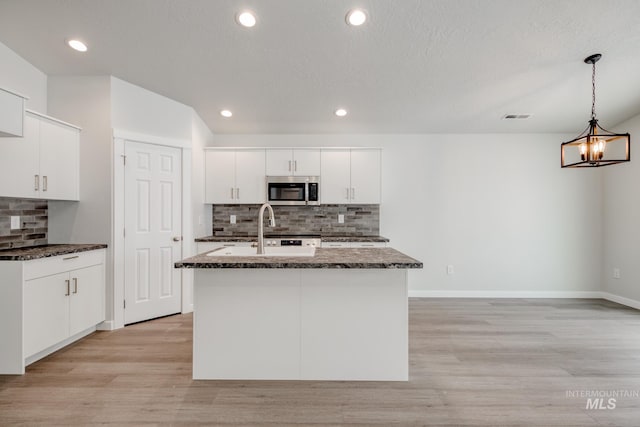 kitchen with dark stone countertops, visible vents, light wood finished floors, a sink, and stainless steel microwave