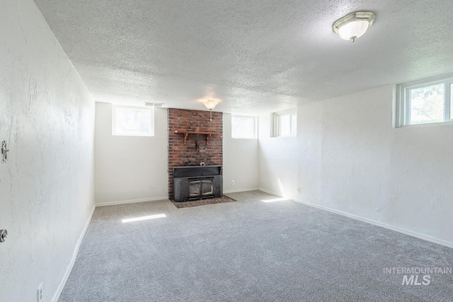 basement with a textured ceiling, carpet floors, a healthy amount of sunlight, and a wood stove