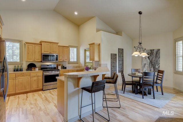 9407 W Pebblestream Dr, Boise, ID 83709 - kitchen with appliances with stainless steel finishes, light brown cabinets, a kitchen breakfast bar, tile countertops, and light wood-style flooring