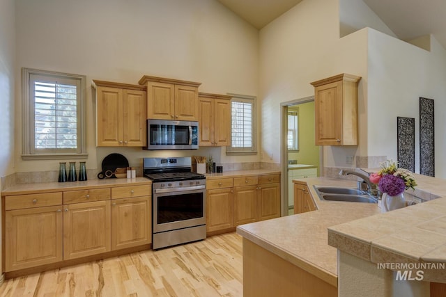 9407 W Pebblestream Dr, Boise, ID 83709 - kitchen with stainless steel appliances, high vaulted ceiling, light countertops, light brown cabinets, and light wood-style floors
