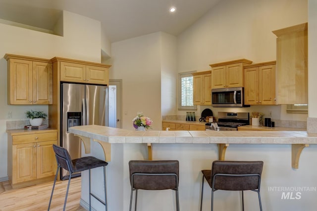 9407 W Pebblestream Dr, Boise, ID 83709 - kitchen with appliances with stainless steel finishes, high vaulted ceiling, light brown cabinetry, a kitchen bar, and a peninsula