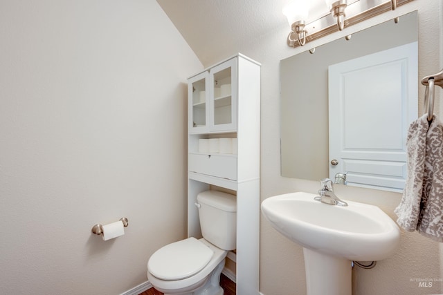 half bath featuring toilet, baseboards, and a sink