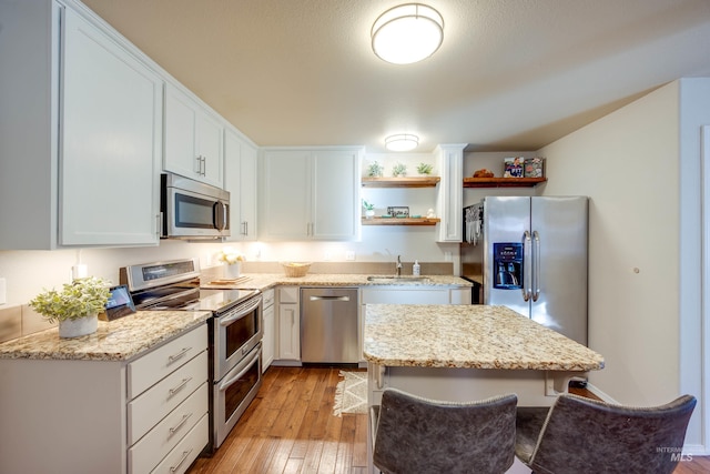 kitchen featuring white cabinets, light wood-style flooring, stainless steel appliances, open shelves, and a sink