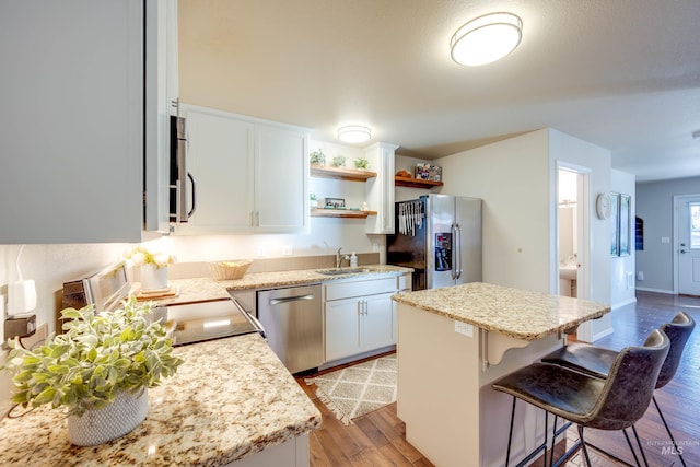 kitchen with appliances with stainless steel finishes, a center island, light wood-style floors, a kitchen bar, and a sink