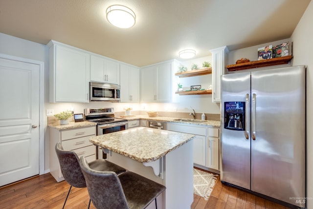 kitchen with a center island, open shelves, appliances with stainless steel finishes, light wood-style floors, and a sink