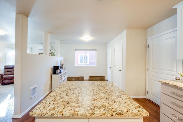 kitchen featuring a center island, visible vents, dark wood finished floors, and light stone countertops