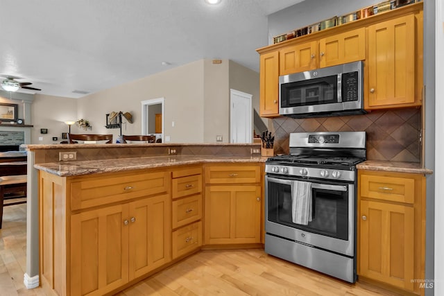 1390 E Prohaska Ct, Eagle, ID 83616 - kitchen with appliances with stainless steel finishes, a peninsula, a ceiling fan, light wood-type flooring, and backsplash