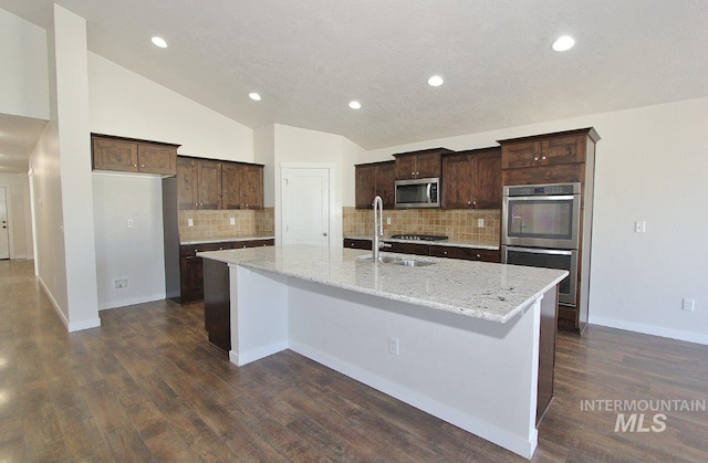 kitchen featuring lofted ceiling, sink, light stone counters, a center island with sink, and appliances with stainless steel finishes