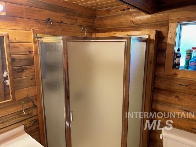 bathroom featuring wooden walls, a shower with door, wooden ceiling, and toilet