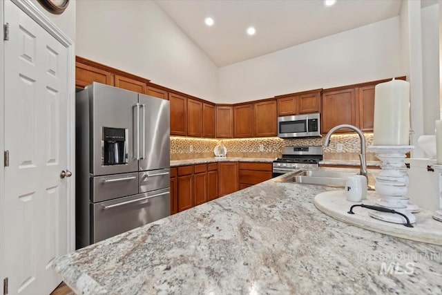 3499 S Green Basin Way, Nampa, ID 83686 - kitchen with stainless steel appliances, decorative backsplash, high vaulted ceiling, brown cabinetry, and recessed lighting