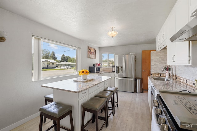 1520 R St, Heyburn, ID 83336 - kitchen with appliances with stainless steel finishes, a sink, exhaust hood, a kitchen breakfast bar, and light wood-type flooring