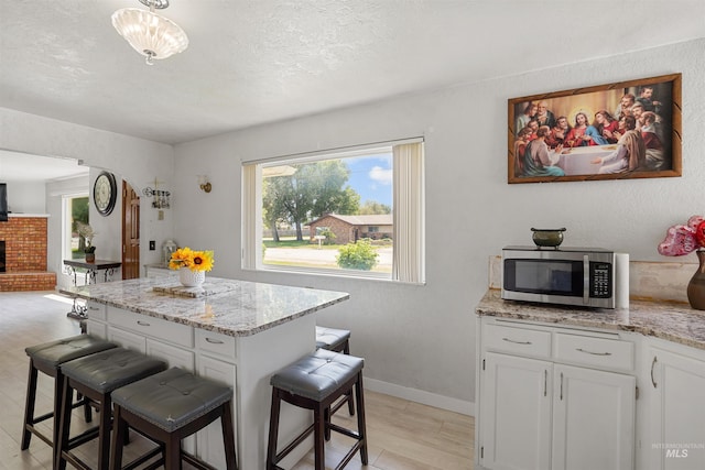 1520 R St, Heyburn, ID 83336 - kitchen featuring stainless steel microwave, plenty of natural light, a breakfast bar area, white cabinetry, and a textured ceiling