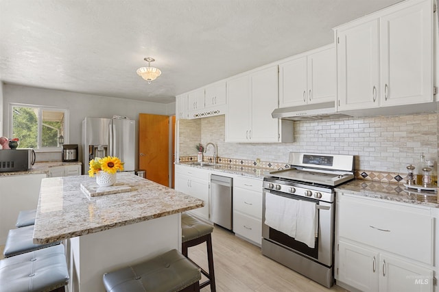 1520 R St, Heyburn, ID 83336 - kitchen with appliances with stainless steel finishes, under cabinet range hood, a breakfast bar, decorative backsplash, and white cabinets
