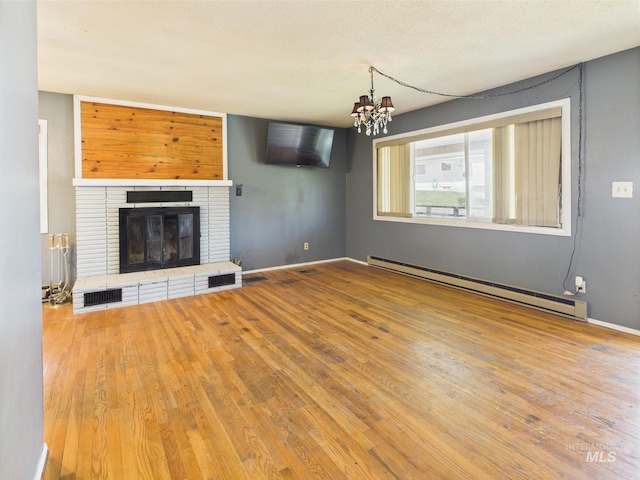 143 Timberline Dr, Pierce, ID 83546 - unfurnished living room featuring baseboard heating, a brick fireplace, wood finished floors, and a notable chandelier