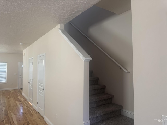 stairs featuring a textured ceiling, wood finished floors, and baseboards