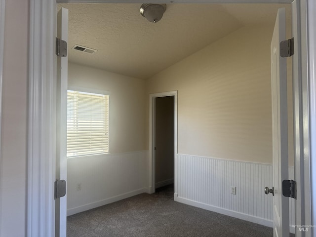 empty room with lofted ceiling, a textured ceiling, baseboards, visible vents, and dark carpet