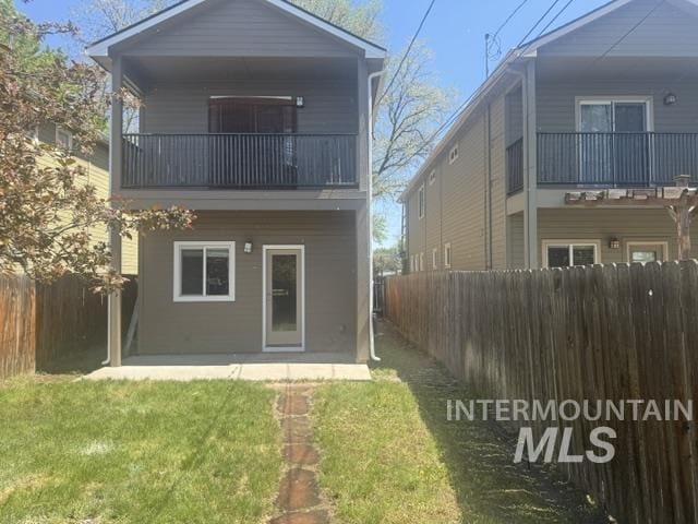 back of house with a fenced backyard, a lawn, and a balcony