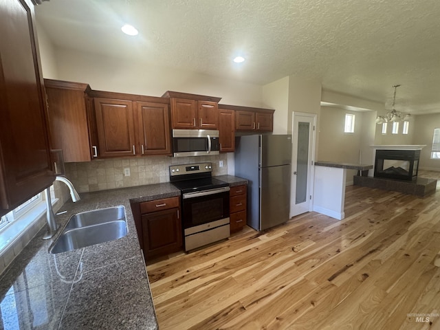 kitchen featuring a textured ceiling, a sink, backsplash, stainless steel appliances, and light wood-type flooring