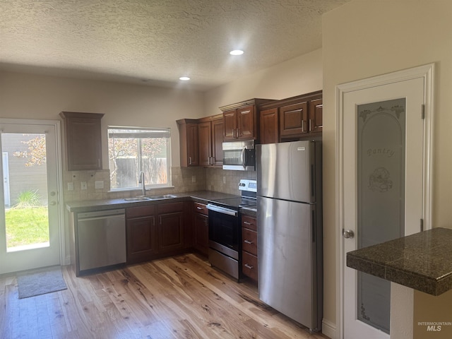 kitchen with a textured ceiling, a sink, backsplash, stainless steel appliances, and light wood-type flooring