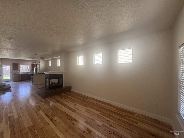 unfurnished living room with a multi sided fireplace, a textured ceiling, wood finished floors, and baseboards