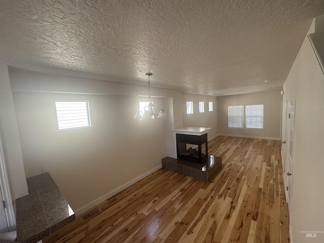 unfurnished dining area featuring light wood finished floors, a multi sided fireplace, a textured ceiling, and baseboards