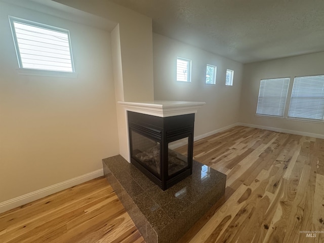 unfurnished living room with baseboards, light wood-style flooring, and a multi sided fireplace