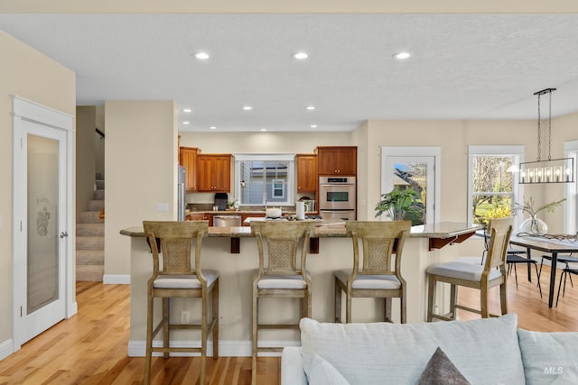 kitchen featuring a kitchen bar, stainless steel appliances, light hardwood / wood-style floors, a textured ceiling, and decorative light fixtures